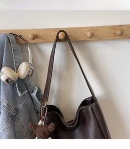 Détail du cabas marron foncé avec breloque ours en peluche sur un crochet en bois