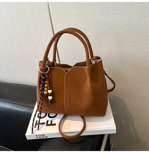 Detail of brown suede handbag featuring V-cut edge and wooden bead charm accessories