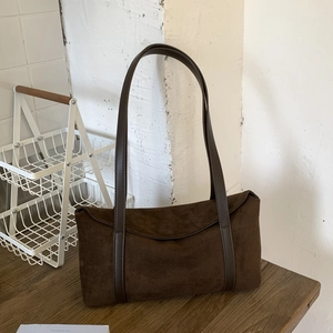 Detail of a dark brown rectangular suede shoulder bag with long straps on a wooden table
