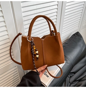 Detail view of a vintage brown bucket bag with decorative stitching and beaded charm