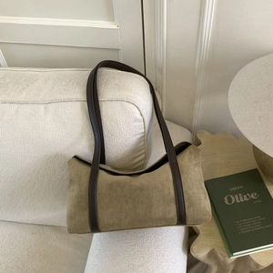 Detail of khaki suede shoulder bag with brown leather strap on a textured white sofa