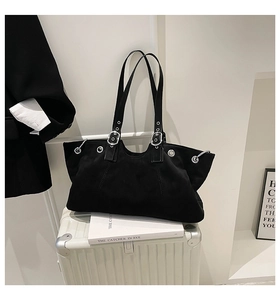 Retro black tote bag with silver metal eyelets placed on a suitcase in a stylish setting