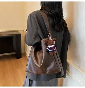 Détail d'un sac seau marron foncé avec bandoulière et un charmant petit ours en peluche