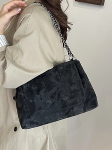 Sac fourre-tout noir rétro à texture mate et bandoulière chaîne porté sur un trench-coat
