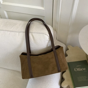 Detail of a brown suede rectangular shoulder bag resting on a white fabric sofa