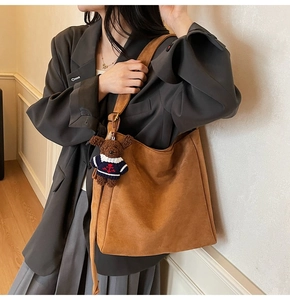 Détail du sac seau en daim marron avec un pendentif ours et une bandoulière réglable