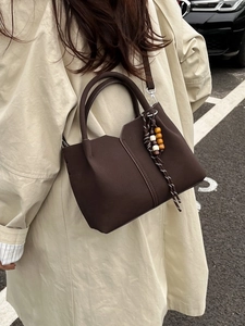 Retro dark brown bucket bag with unique folding structure and tassel charm on street