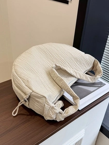 Chic beige pleated crescent tote bag with knot strap detail on a dark wood surface