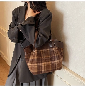 Détail d'un sac cabas vintage à carreaux avec poignées en cuir marron porté par un mannequin