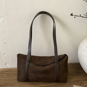 Detail of dark brown suede pillow bag with long leather strap on a rustic wooden surface