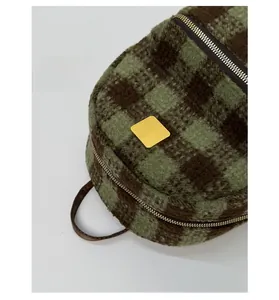 Detailed close-up of premium gold hardware and green plaid plush texture on the backpack