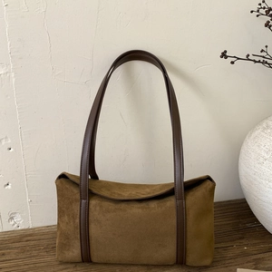 Detailed close-up of brown suede pillow bag on vintage wood with minimalist ceramic vase