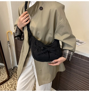 Gros plan du sac croissant plissé noir avec décoration nœud sur trench-coat kaki