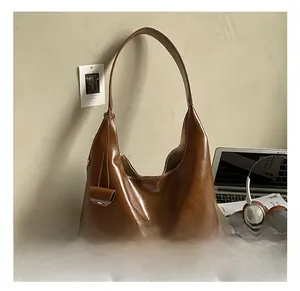 Brown leather hobo tote bag detail with detachable mini pouch on a modern desk