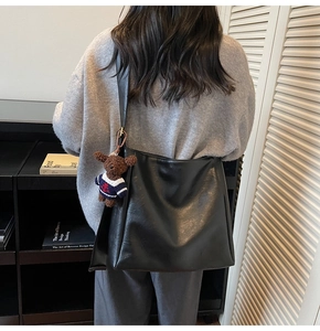 Détail d'un grand sac seau en daim noir avec un pendentif ours et une bandoulière