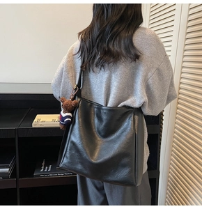 Détail du sac seau noir mat porté par le mannequin avec un charmant ours en peluche