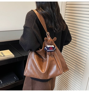 Vue latérale d'un sac seau en cuir mat marron avec un joli pendentif ours en peluche