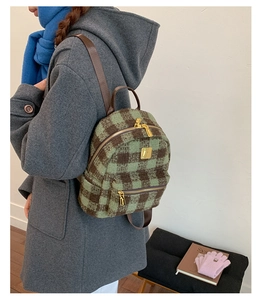 Detail of green and brown plaid winter backpack with gold zippers worn on a wool coat