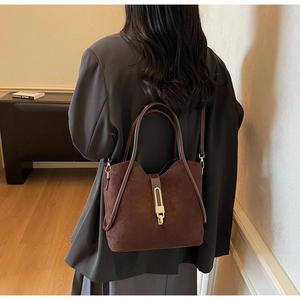 Detail of a dark brown suede tote bag with elegant gold metal bar clasp and slim strap