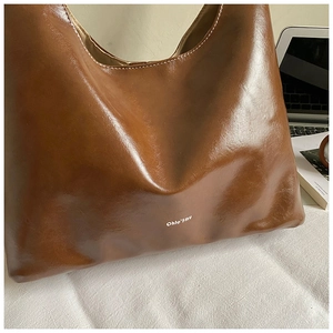Detail of caramel leather tote bag showing white stitching and brand logo texture