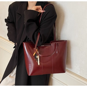 Dettaglio borsa tote in pelle lucida bordeaux con ciondolo decorativo in perle di legno