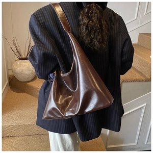 Detail of a deep brown hobo bag worn with a navy blazer, showing the glossy patent finish