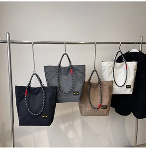 Detail showing four waterproof nylon tote bags in black, grey, khaki and white on hangers