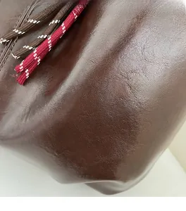 Detail of soft brown textured leather with decorative woven ropes on a large hobo bag