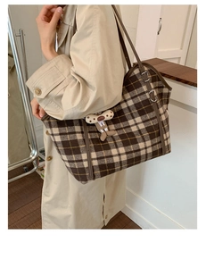 Detail of checkered tote bag featuring brown leather strap and plush cartoon pendant charm