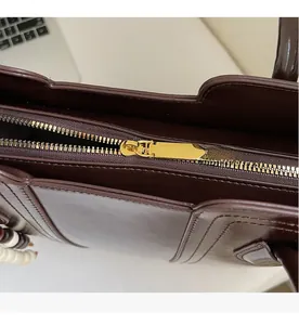 Detail of smooth golden metal zipper on a dark brown textured leather tote bag