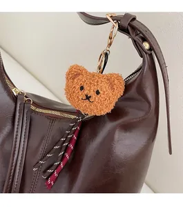 Detail of bear plush charm with brown textured tassel on a dark brown leather bag