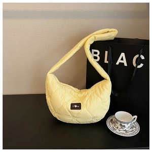 Détail du sac croissant matelassé jaune clair avec texture cœur et étiquette en perle