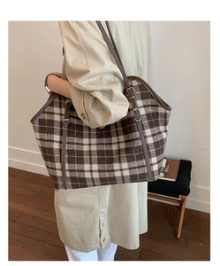 Detail view of large tote bag featuring brown plaid pattern and metallic buckles on straps