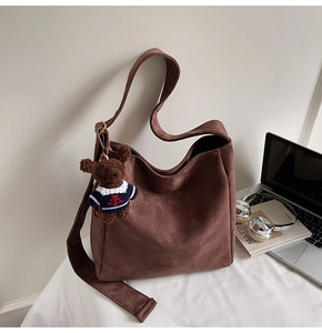 Détail d'un sac seau en daim marron avec pendentif ours sur un bureau blanc
