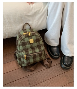 Detail of green and brown plaid mini backpack with golden zipper on a wooden floor