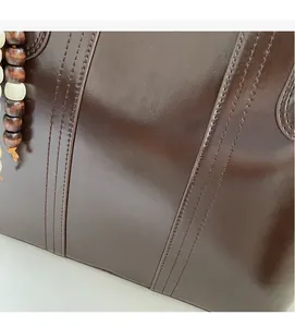 Detailed macro view of smooth brown leather tote with fine stitching and wooden bead charm
