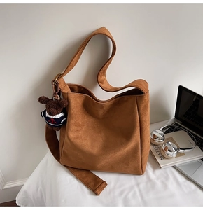 Détail du sac seau en daim marron caramel avec un charm ours sur une parure de lit blanche