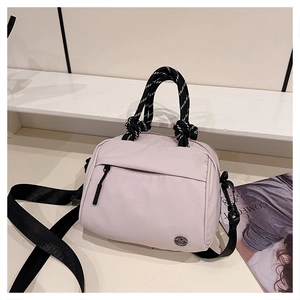 Detail of light pink crossbody bag featuring woven rope handles and adjustable strap