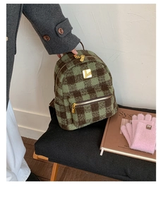Detail view of plaid wool backpack with golden metal logo and front zipper pocket