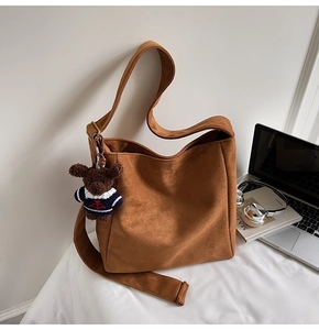 Détail d'un sac seau en daim marron avec pendentif ours et large bandoulière au bureau