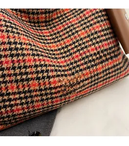 Close-up of houndstooth wool fabric texture and metal brand plate on the shoulder bag