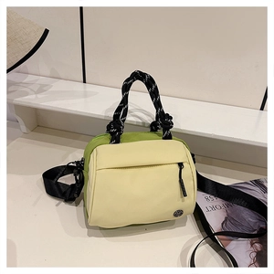 Detail of color-block nylon tote bag with braided handle and adjustable strap on white table