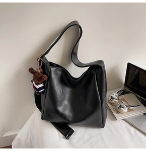 Détail d'un sac seau noir mat avec un charm d'ours marron tricoté et une longue bandoulière