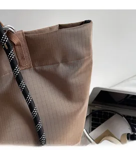 Detail of the waterproof ripstop fabric and woven checkered handles on this brown tote bag