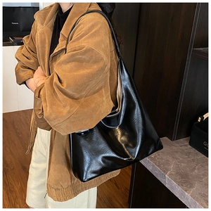 Close-up of black glossy leather tote bag with wide strap on shoulder of model