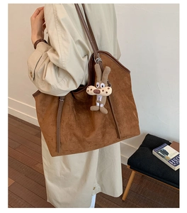 Detail view of large brown tote bag with leather straps and cute rabbit charm
