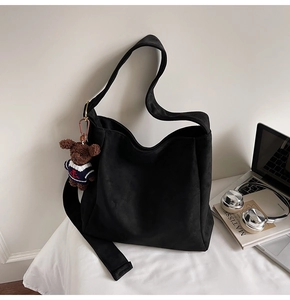 Détail du sac seau en daim noir mat avec breloque ours et large bandoulière réglable