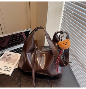 Detail of dark brown leather tote bag featuring a cute bear charm and metal zipper
