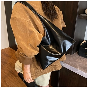Black glossy patent leather tote bag shown on shoulder over a camel suede jacket