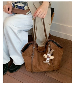 Brown suede tote bag with cartoon rabbit charm and adjustable shoulder strap detail